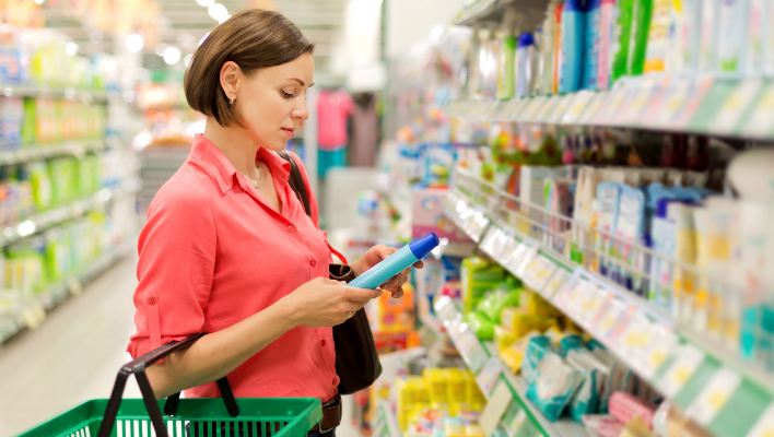femme regardant l'étiquette d'une bouteille de shampoing dans un supermarché